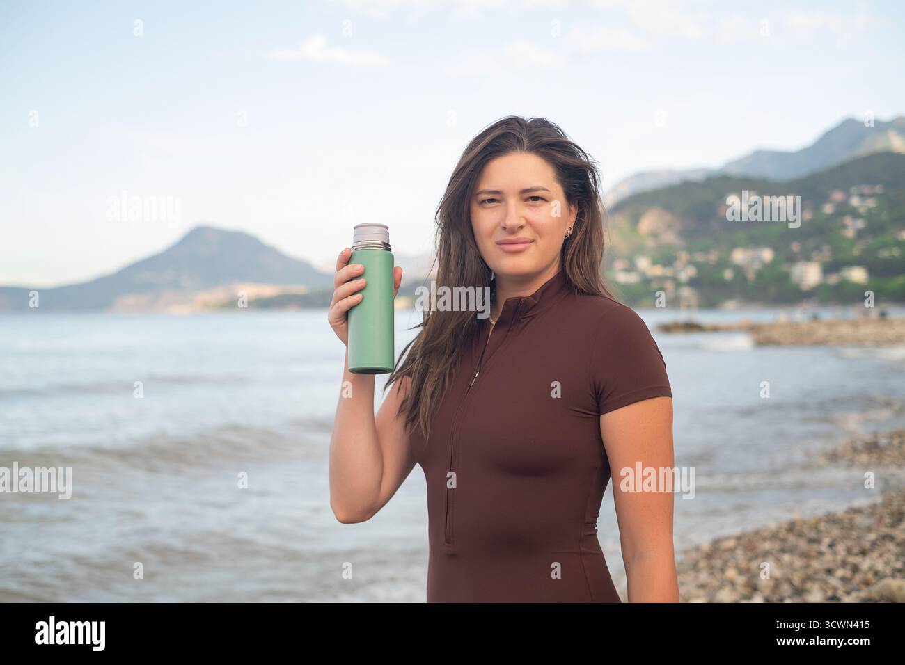 Gesunder Morgen am Meer. Sportliche Frau, die nach dem Training Feuchtigkeit spendet und entspannt. Stockfoto