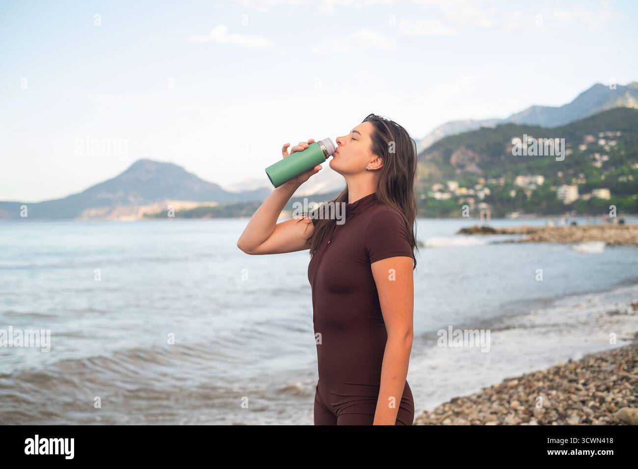 Morgendliche Fitness am Meer. Frau lädt Energie und Trinkwasser nach dem Training auf. Stockfoto