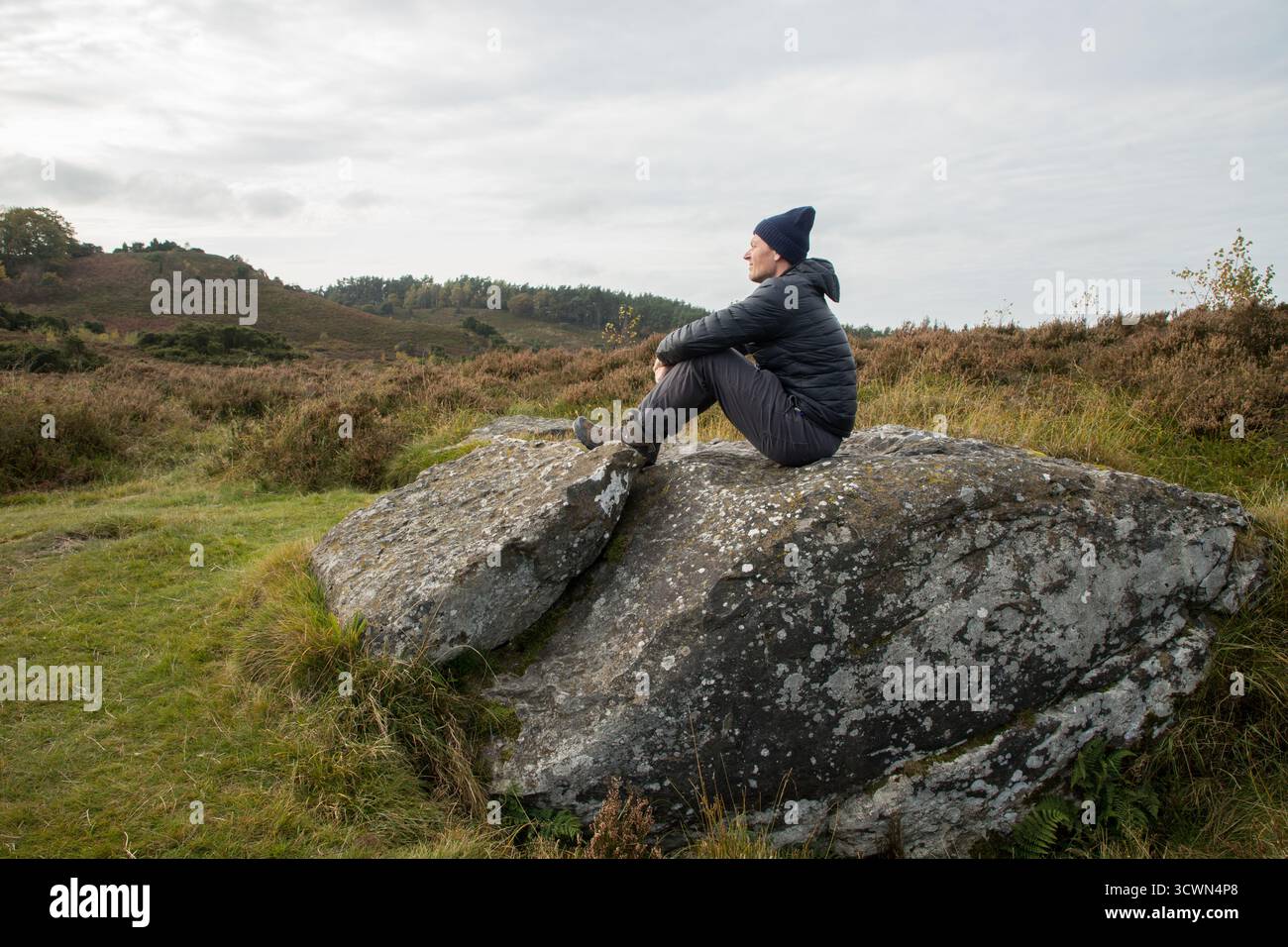 Mann, der im Herbst auf großen Felsen in flacher Heidefläche sitzt und den ruhigen Moment allein in der Natur genießt Stockfoto