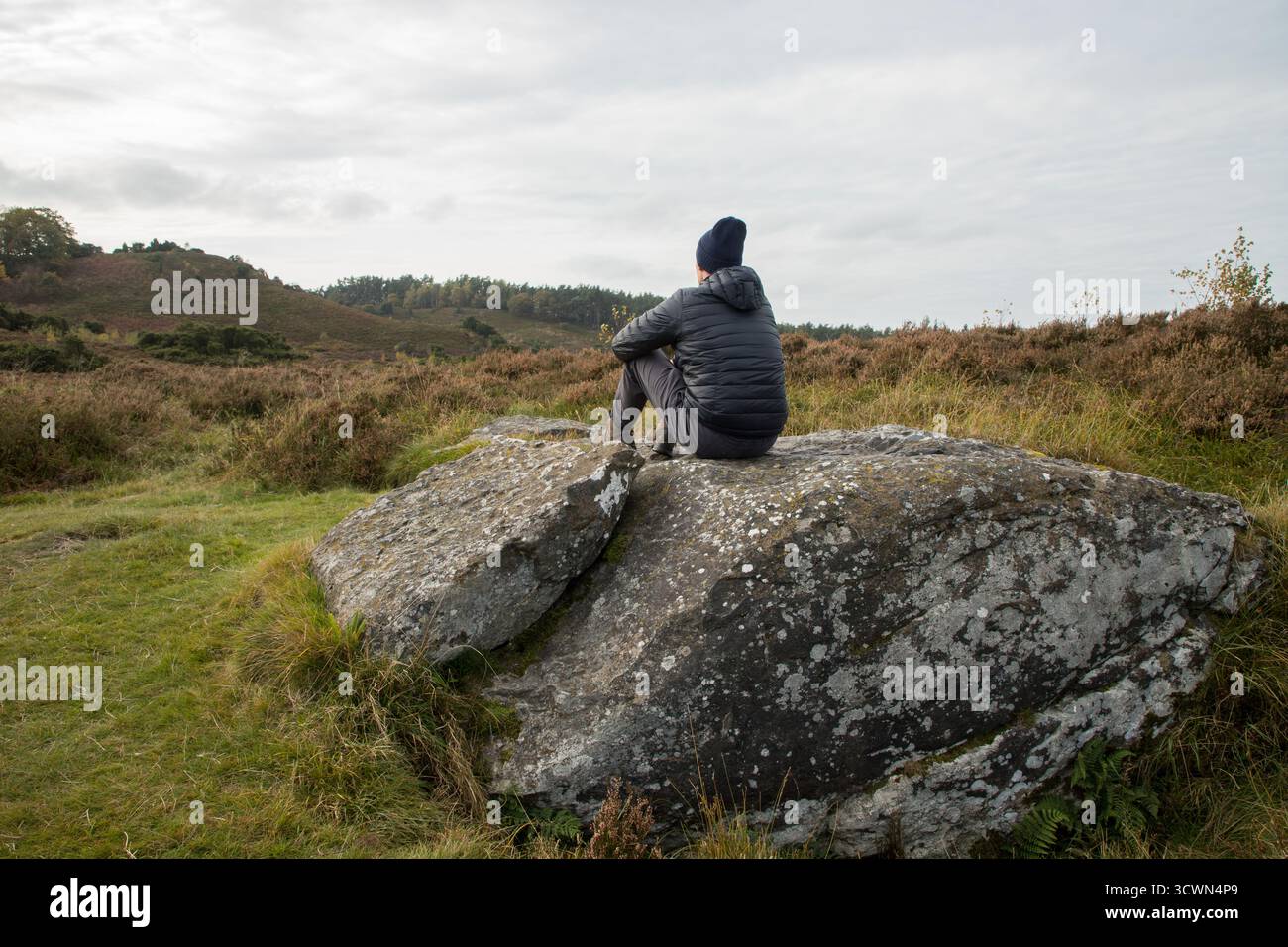 Mann, der im Herbst auf großen Felsen in flacher Heidefläche sitzt und den ruhigen Moment allein in der Natur genießt Stockfoto