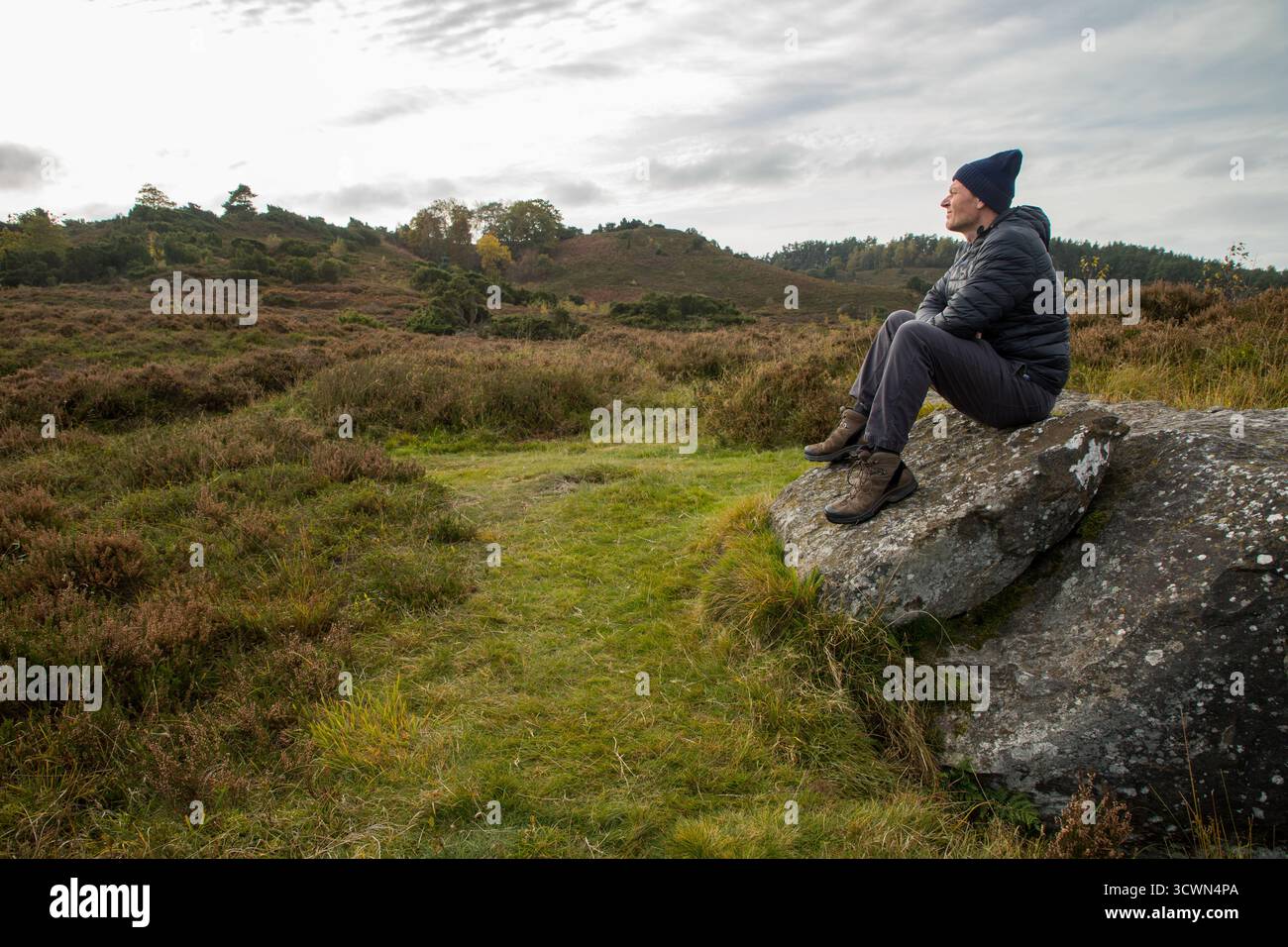 Mann, der im Herbst auf großen Felsen in flacher Heidefläche sitzt und den ruhigen Moment allein in der Natur genießt Stockfoto