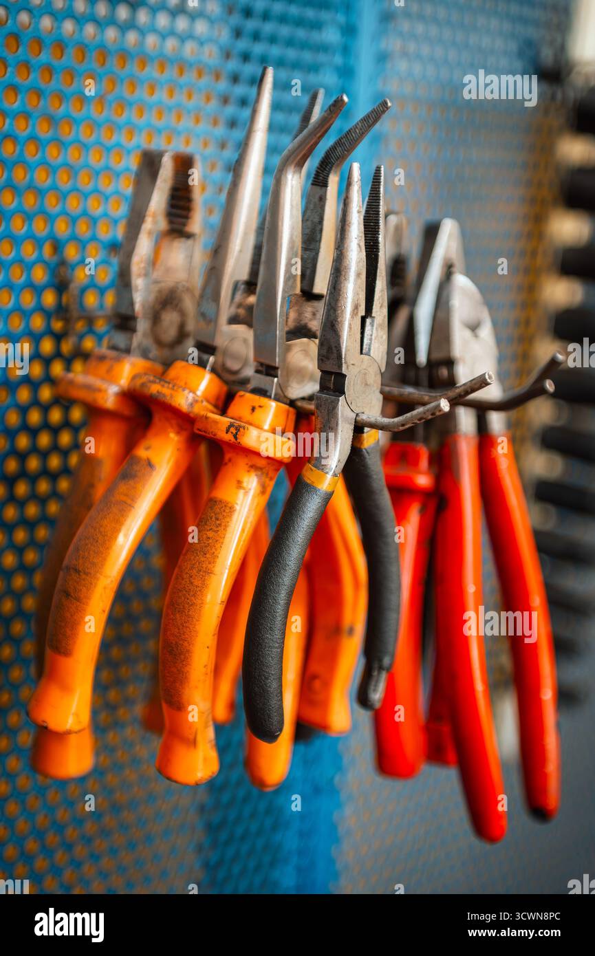 Zangen und verschiedene Handwerkzeuge hängen an einer Werkbankwand in einer Werkstattgarage Stockfoto