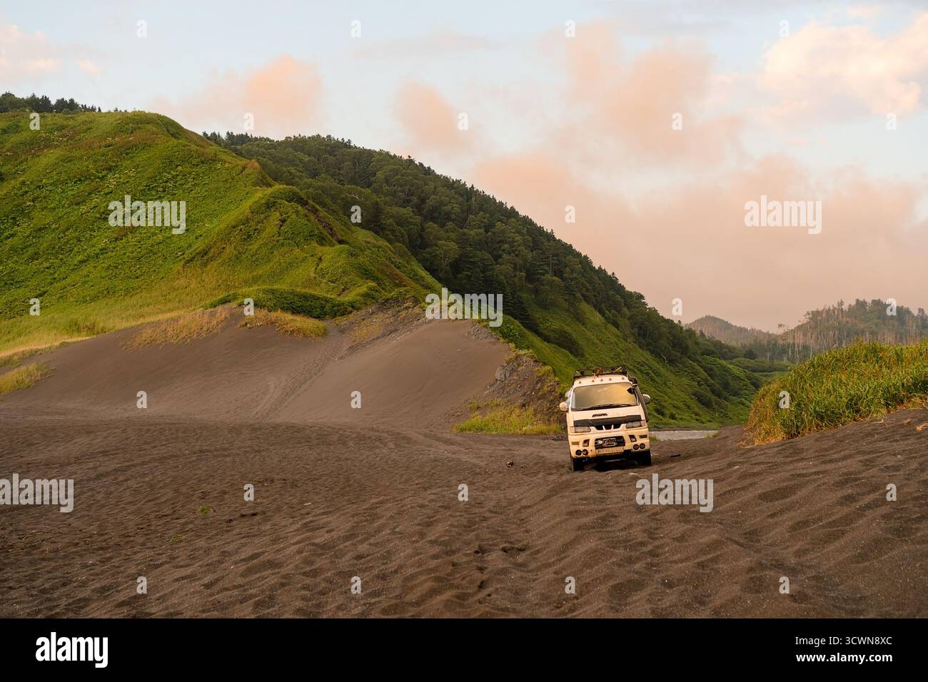 Das robuste Expeditionsfahrzeug steht allein am unberührten Strand mit dramatischen Bergkämmen, die auf das Meer treffen. Ideal für Abenteuertourismus und Transporterlebnisse. Stockfoto