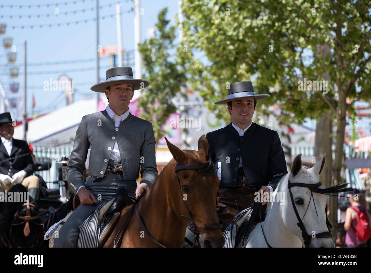 Sevilla, Spanien - 23. April: Zwei Männer in traditioneller Kleidung reiten auf einer Messe, mit festlichem Hintergrund Stockfoto