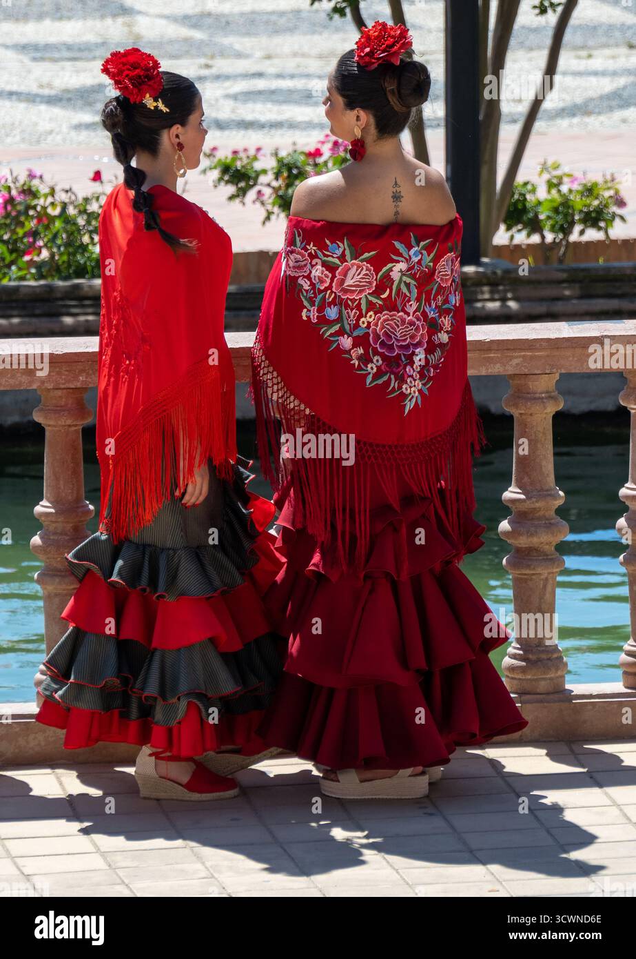Sevilla, Spanien - 23. April: Zwei Frauen in traditionellen roten Kleidern mit Rüschen und Blumenstickerei, die an einem Wasserkörper stehen und kulturelle Akzente zeigen Stockfoto