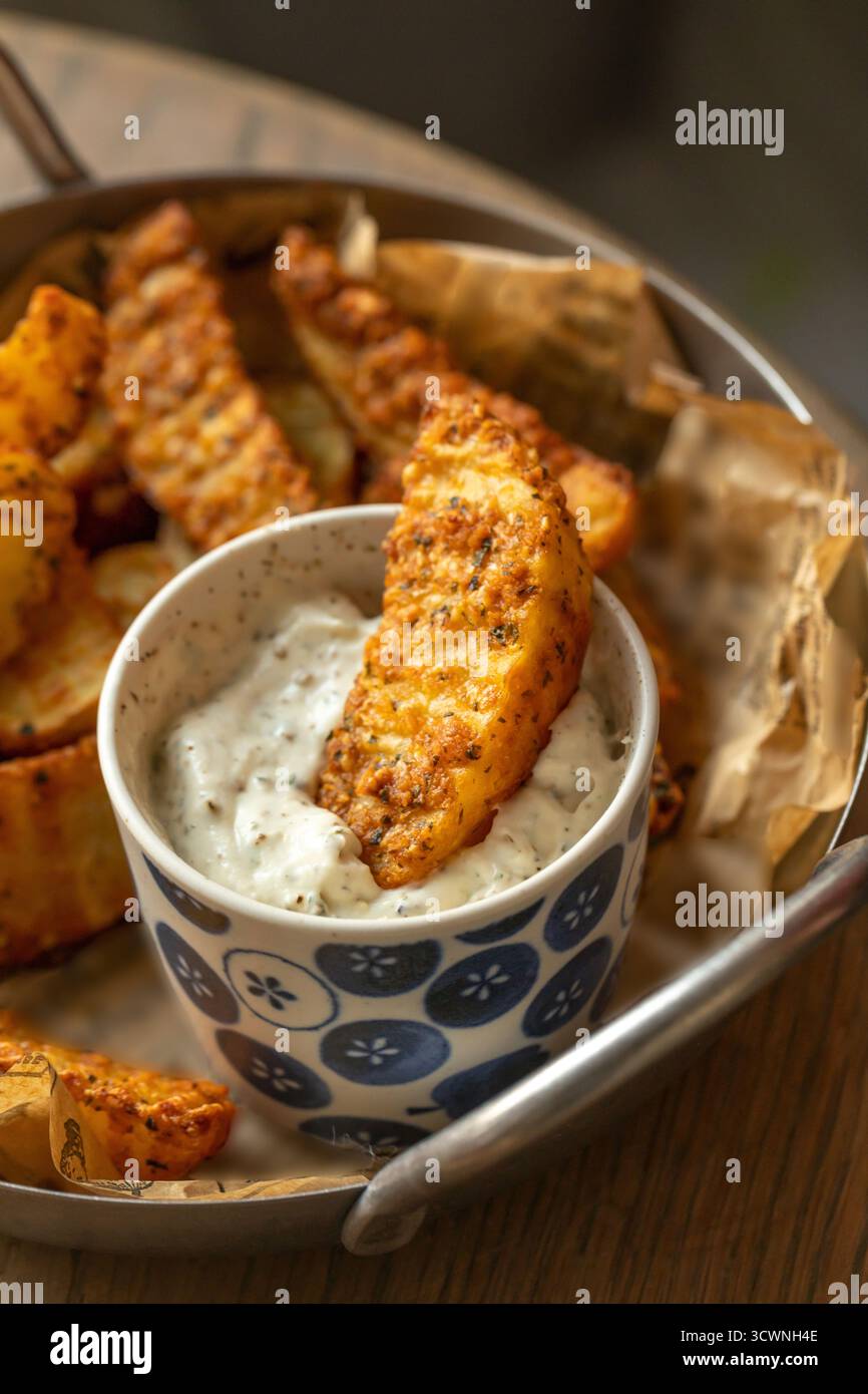 Knusprig gewürzte Kartoffelscheiben mit cremigem Kräuterdip, gebratene Kartoffelscheiben mit Tatarensauce. Selektiver Fokus Stockfoto