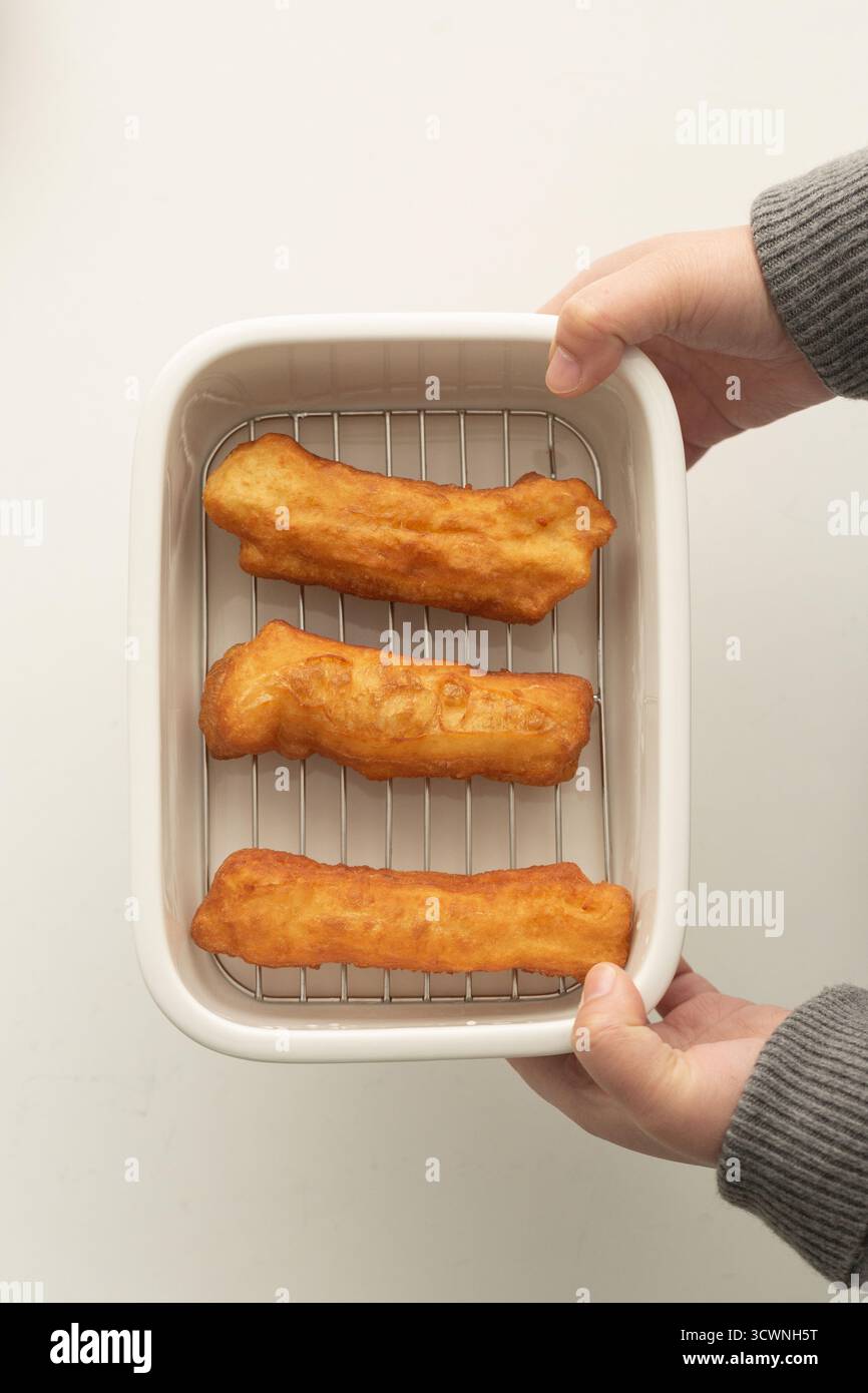 Hände halten ein Tablett mit frisch gebratenem Youtiao, vietnamesischen Teigstäbchen, gebratenen Käsestäbchen in einem weißen Plastikbehälter auf weißem Hintergrund Stockfoto
