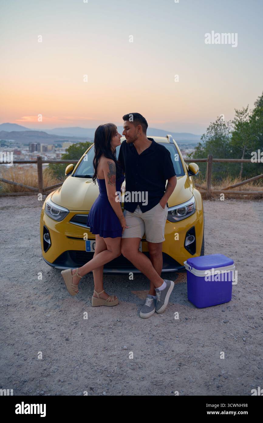 Liebevolles Paar, das sich während eines Roadtrips bei Sonnenuntergang umschließt Stockfoto