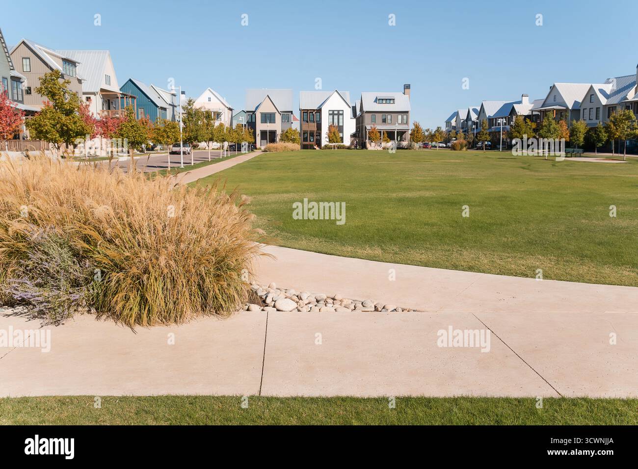 Grasbewachsener Nachbarschaftspark umgeben von modernen Häusern und Bürgersteigen. Stockfoto
