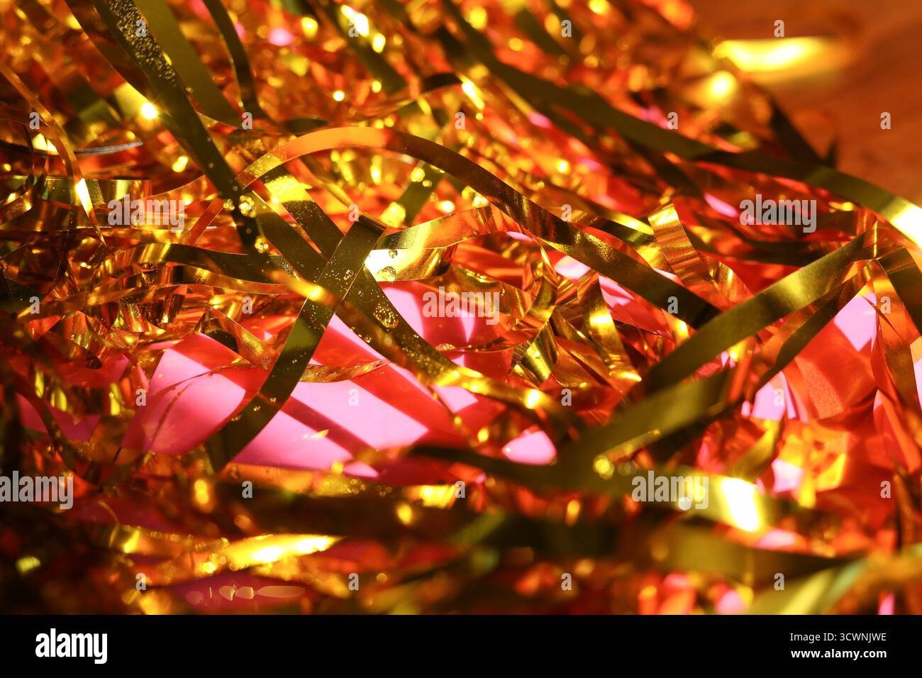 Nahaufnahme von Goldlametta mit Sekttropfen vor rosa Hintergrund Stockfoto