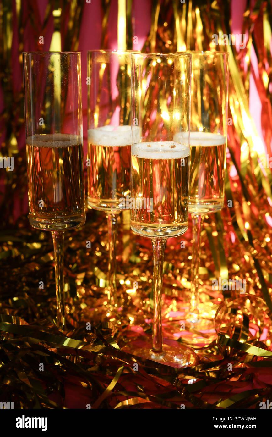 Gruppe prickelnder Champagnerflöten auf goldenem Lametta mit rosafarbenem Hintergrund Stockfoto