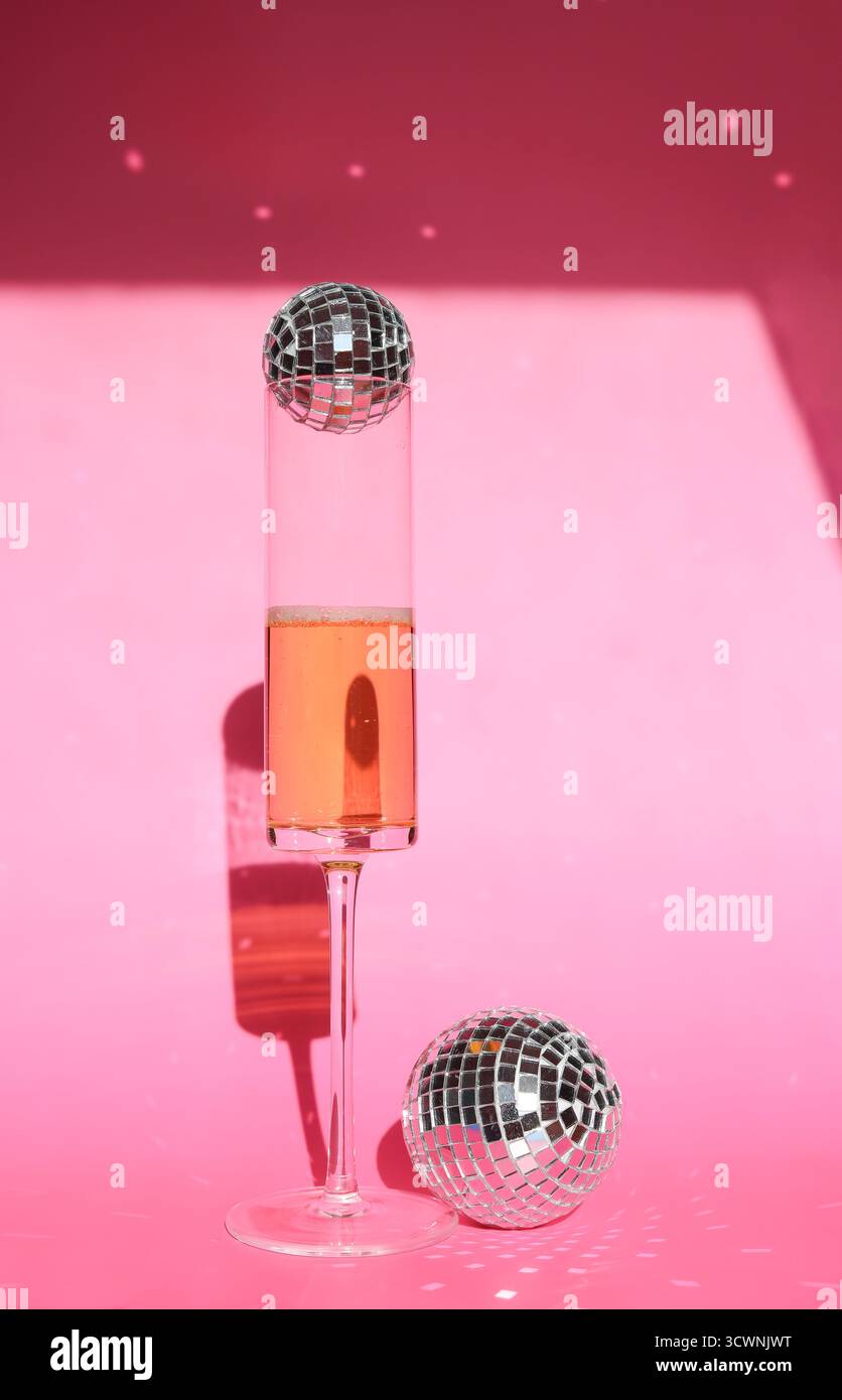 Schickes Champagnerglas vor leuchtendem rosafarbenem Hintergrund mit Discokugeln Stockfoto