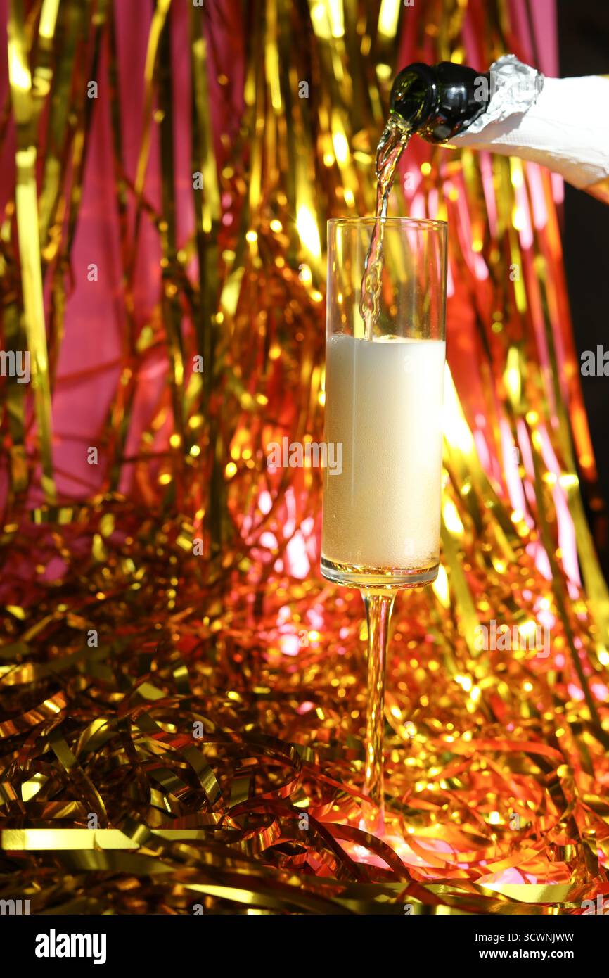 Champagner wird in ein Glas auf glitzerndem goldenen Hintergrund gegossen Stockfoto