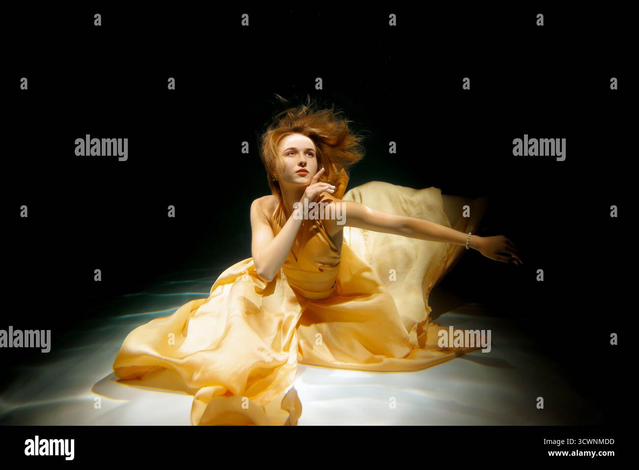 Eine Frau schwimmt anmutig unter Wasser, gekleidet in einem fließenden gelben Kleid Stockfoto