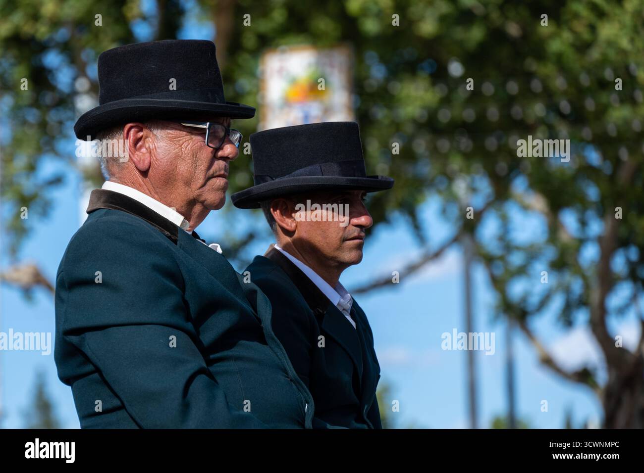 Sevilla, Spanien - 23. April: Zwei Männer mit traditionellen Hüten und formeller Kleidung sitzen nebeneinander, draußen mit Bäumen im Hintergrund Stockfoto