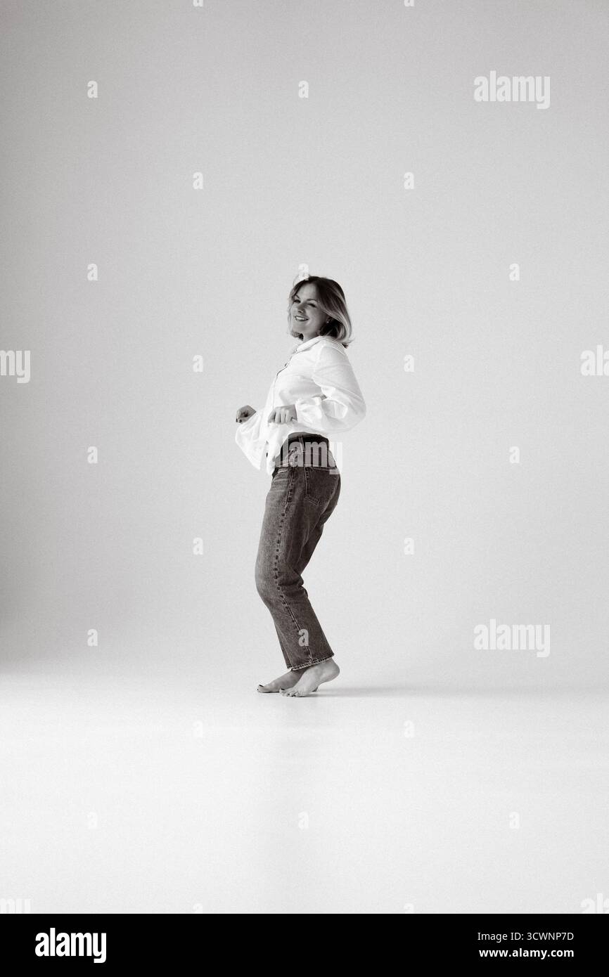 Frau tanzt in weißem Hemd und Jeans, minimalistischer Hintergrund Stockfoto