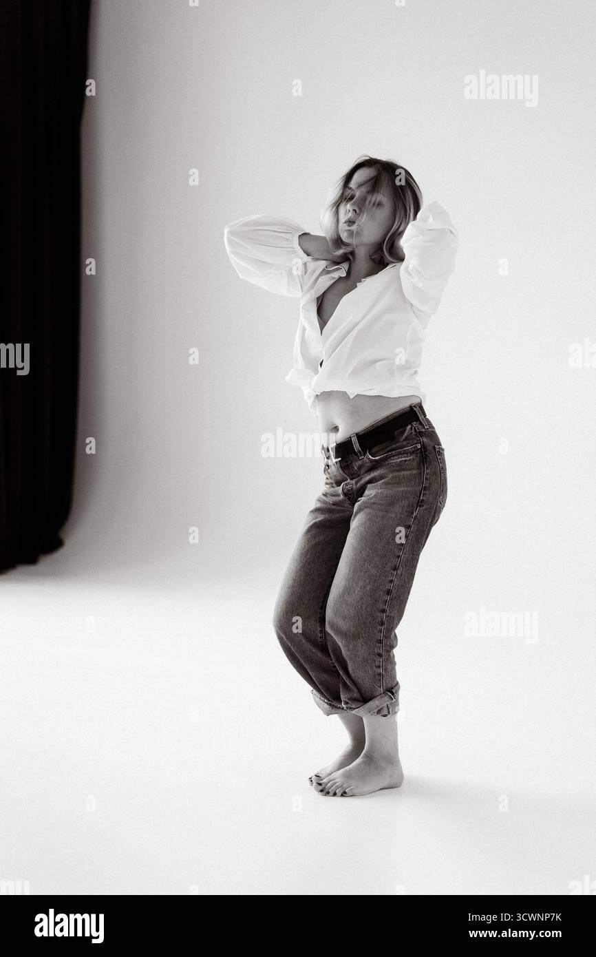Frau tanzt in weißem Hemd und Jeans, minimalistischer Hintergrund Stockfoto