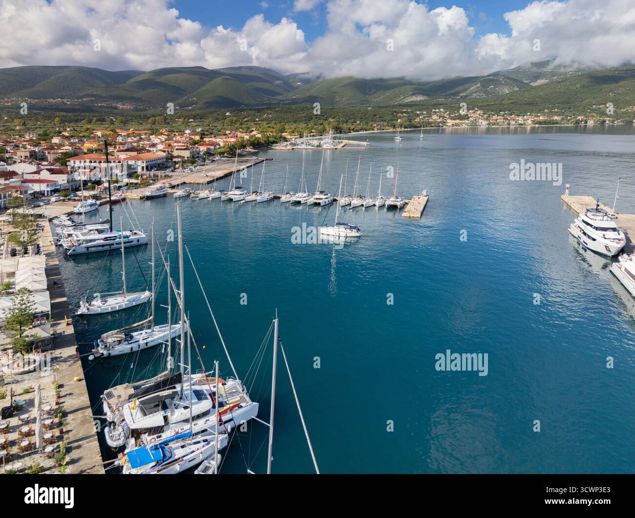 Aus der Vogelperspektive sehen Sie Yachten und Boote, die im türkisfarbenen Wasser des Hafens von Sami ruhen, vor dem Hintergrund grüner Berge und bewölkter Himmel, Sami, Kephalonien, Griechenland. Stockfoto