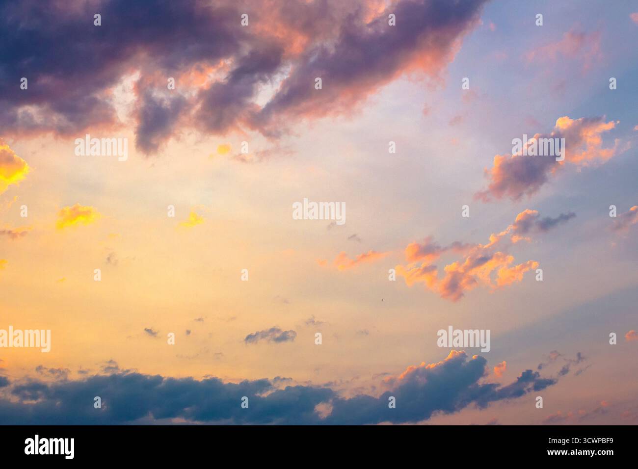 Dunkle Wolkenlandschaft bei Sonnenuntergang. Orange-violette Wolken auf einem gelb-blauen Himmelsverlauf im Abendlicht. Dramatischer Wetterwechsel. Hintergrund der Windvorhersage. Stockfoto