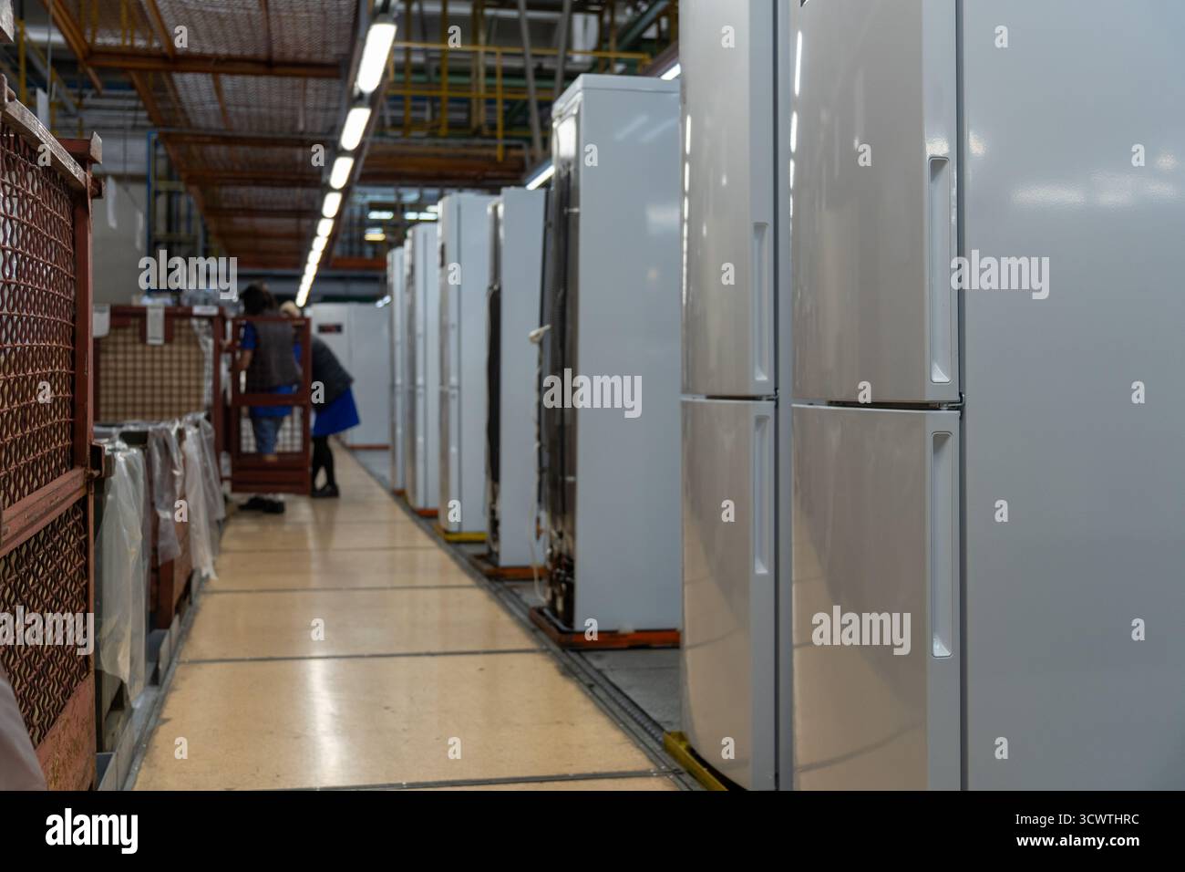 Eine Montagelinie oder ein Lager, die eine Reihe moderner Kühlschränke in einer Fabrik zeigt, mit einem unscharfen Hintergrund von Arbeitern und Industrieanlagen, signif Stockfoto