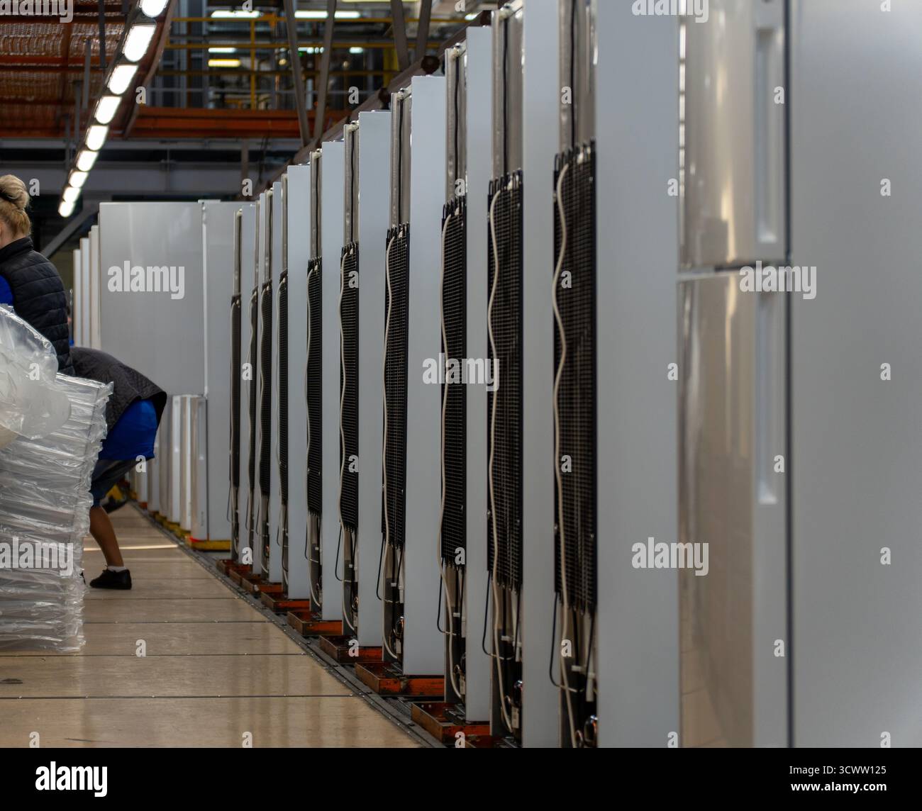 Eine Montagelinie oder ein Lager, die eine Reihe moderner Kühlschränke in einer Fabrik zeigt, mit einem unscharfen Hintergrund von Arbeitern und Industrieanlagen, signif Stockfoto
