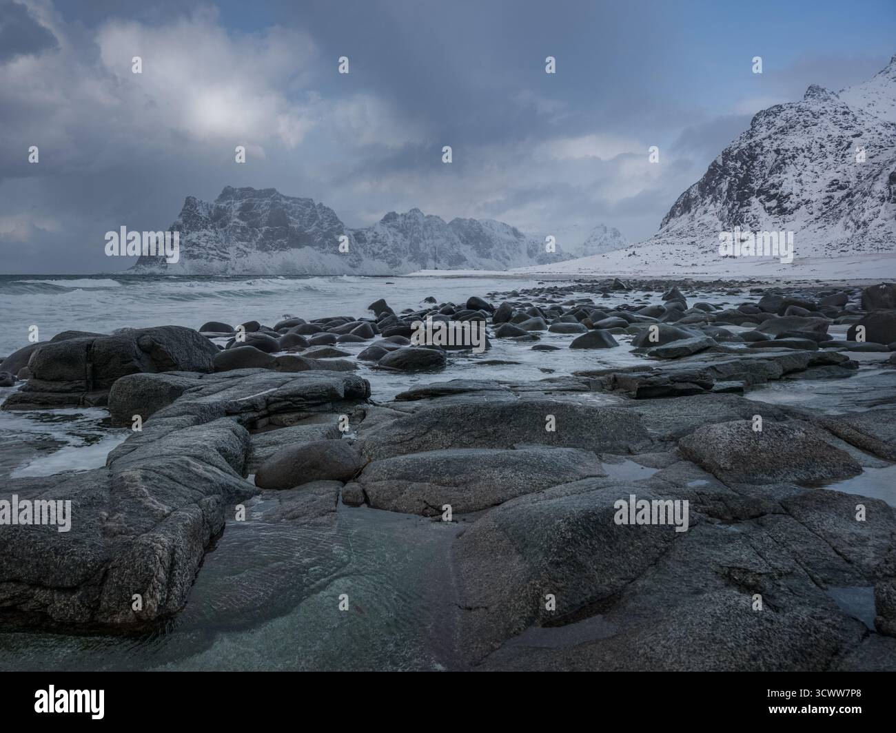 Arktische Meereslandschaft mit schneebedeckten Bergen und gefrorenen Felsen an der Lofoten-Küste unter dem dramatischen Winterhimmel in Nordnorwegen Stockfoto
