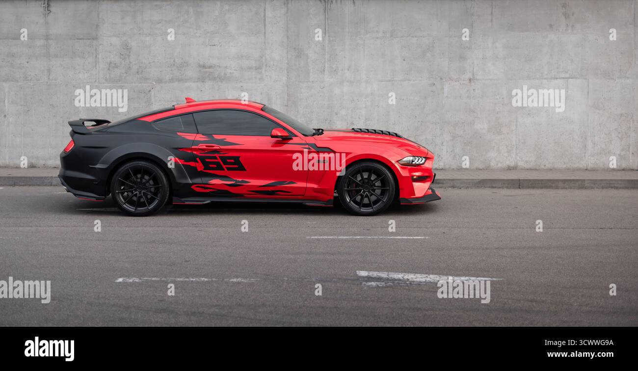 Zweifarbiger Ford Mustang parkte auf einer Straße. Seitenansicht rot und schwarz eines amerikanischen Ponywagens gegen Betonwand. Stockfoto
