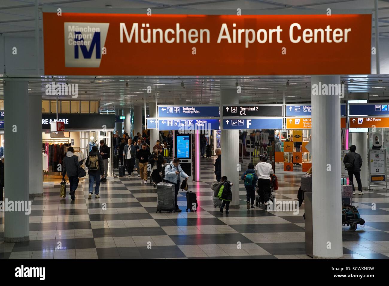 Innenausstattung des Münchner Flughafenzentrums mit Reisenden, Gepäckwagen und deutlicher Beschilderung zwischen Terminal 1 und Terminal 2. München, Deutschland Stockfoto Innenausstattung des Münchner Flughafenzentrums mit Reisenden, Gepäckwagen und deutlicher Beschilderung zwischen Terminal 1 und Terminal 2. München, Deutschland Stockfoto