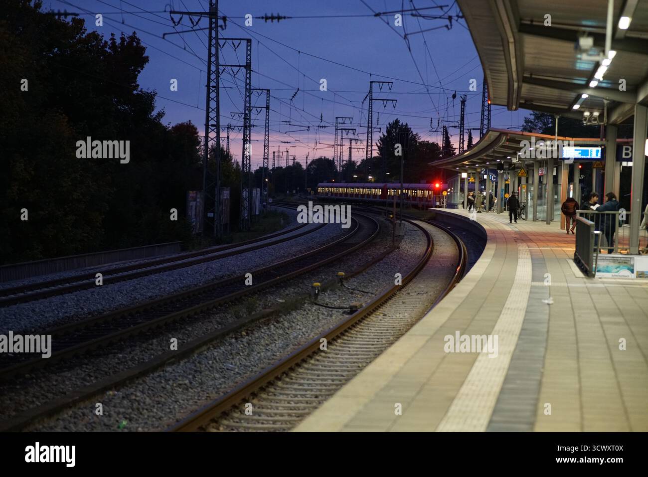 Abendliche Pendlerzüge verlassen den Bahnhof Westkreuz in Berlin in der Abenddämmerung unter sanftem violettem Licht und Oberleitungen. München, Deutschland Stockfoto