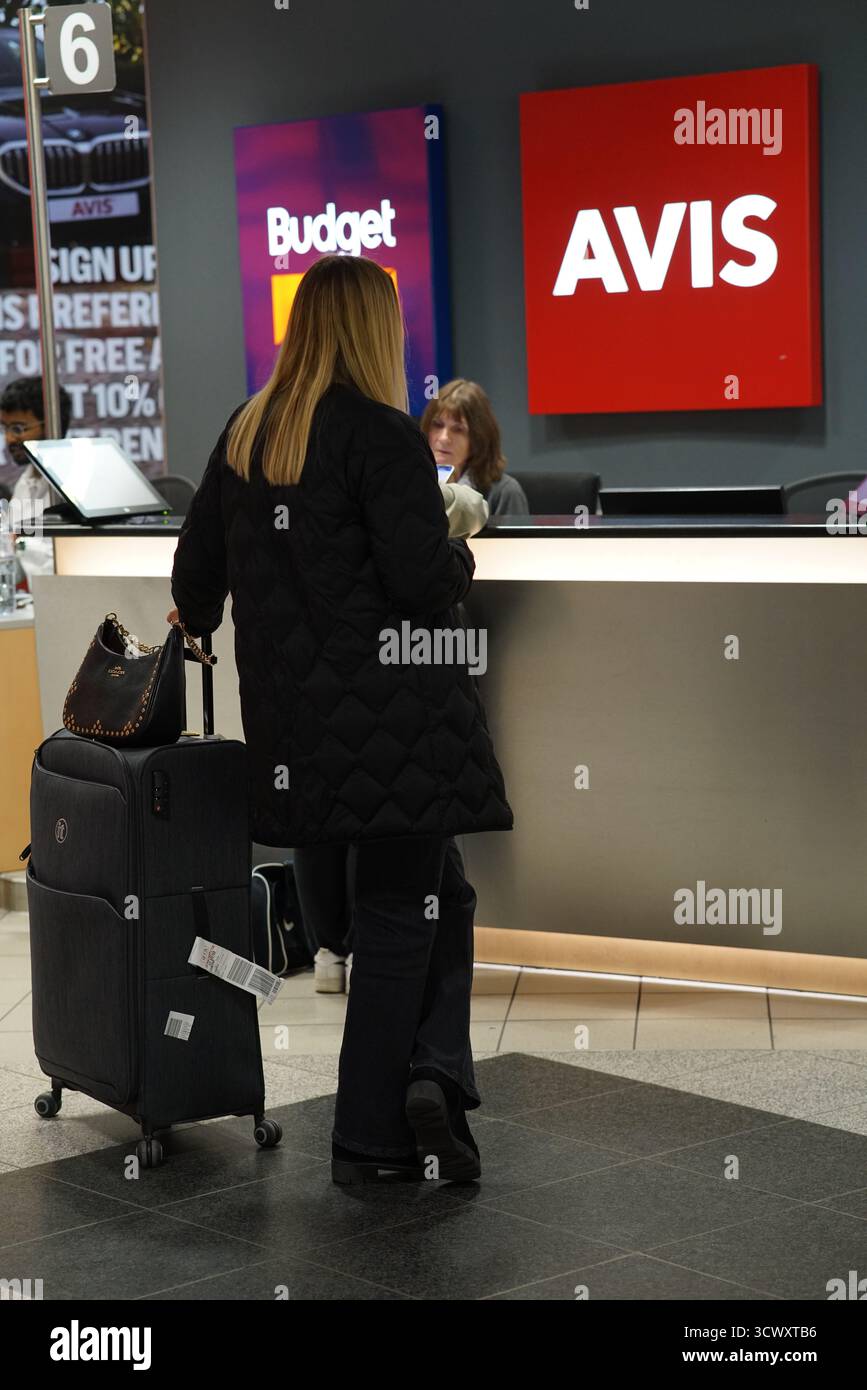 Weibliche Reisende mit Gepäck am Avis and Budget Autovermietungsschalter im Münchner Flughafenterminal. München, Deutschland Stockfoto