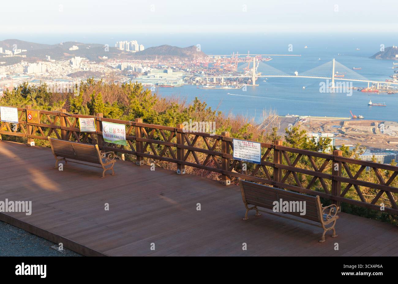 Busan, Südkorea - 13. März 2018: Ein ruhiger Ausblick mit Bänken und einem hölzernen Geländer, der einen geschäftigen Hafen, Hafenanlagen und eine Suspension freigibt Stockfoto