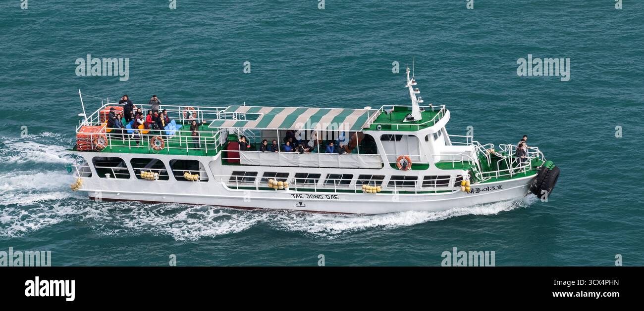 Busan, Südkorea - 18. März 2018: Eine weiße Passagierfähre gleitet mit Gruppen von Reisenden auf dem Oberdeck durch blau-grünes Wasser Stockfoto