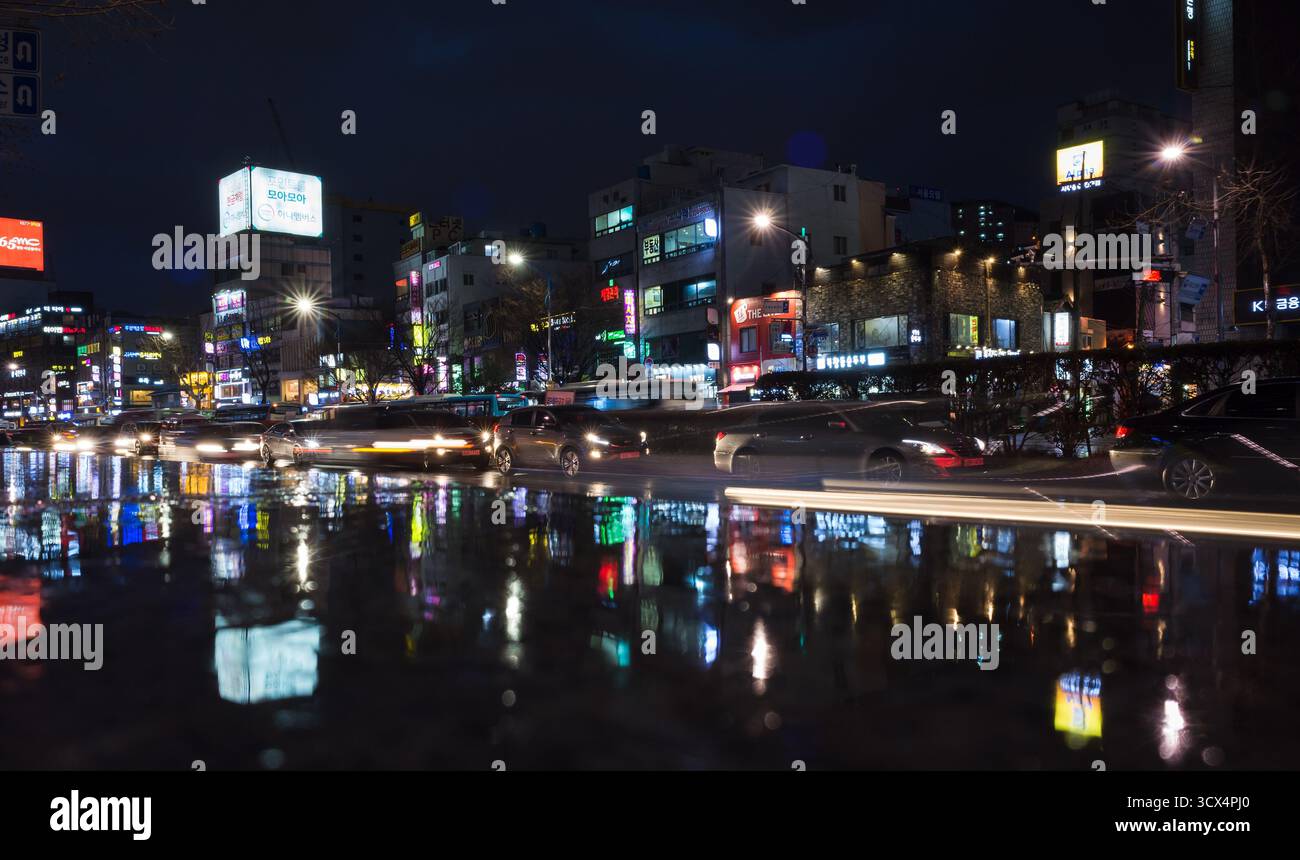 Busan, Südkorea - 19. März 2018: Eine lebhafte nächtliche Szene, in der die Lichter der Stadt auf einer nassen Oberfläche in einer geschäftigen Innenstadt reflektieren Stockfoto