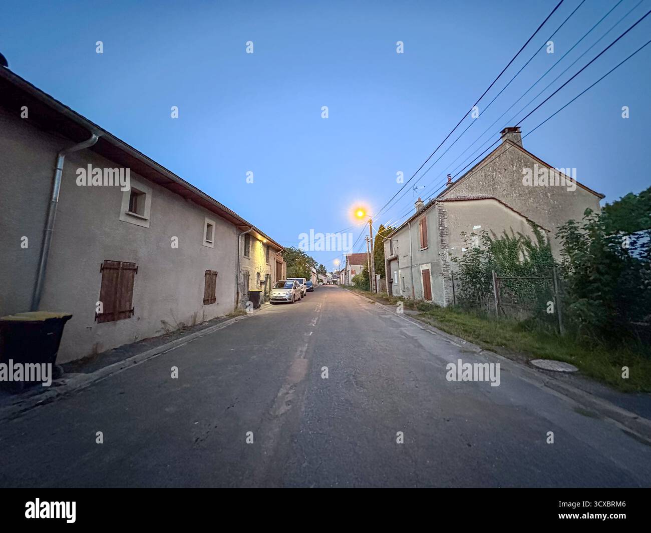 Bergnicourt, Rethel, Ardennes, Grand-Est, Frankreich, August, 28. August 2025, Eine ruhige Dorfstraße in der Abenddämmerung, sanft von Straßenlaternen beleuchtet, die das Wesen des friedlichen ländlichen Charmes einfangen Stockfoto