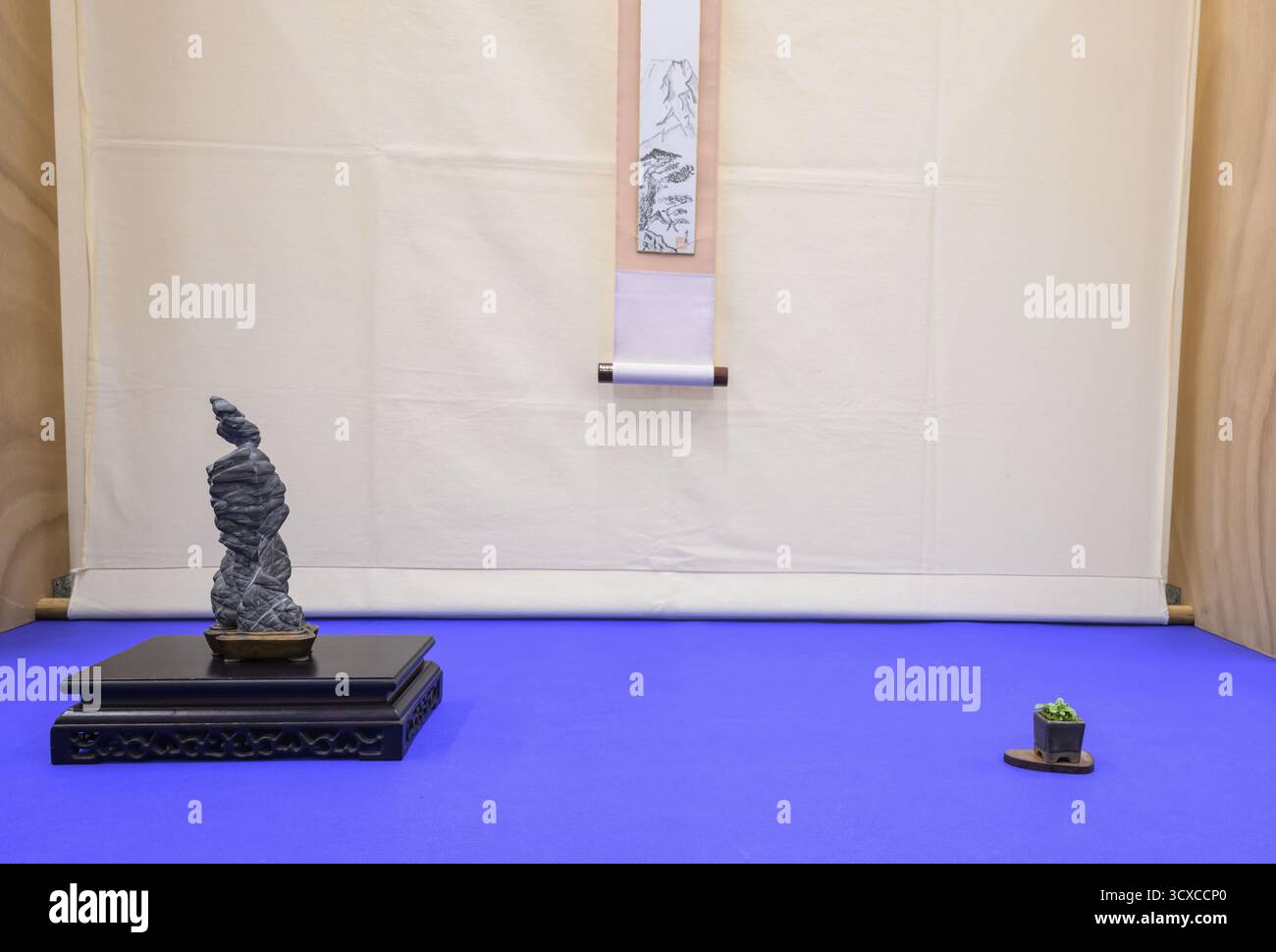 Eine komplexe Suiseki-Steinkunst auf einem Sockel, mit einer Rolle und einer winzigen Pflanze in der Nähe, Italien Stockfoto