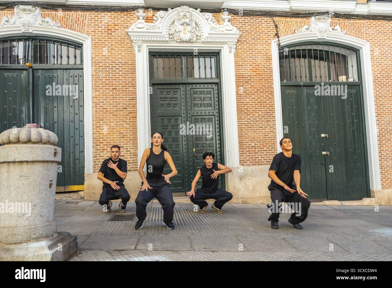 Gruppe von vier dynamischen jungen Tänzern, die synchronisierte künstlerische Choreographie in einer Stadtstraße vorführen, in der Talente und urbane Bewegungen gegen einen bri gezeigt werden Stockfoto
