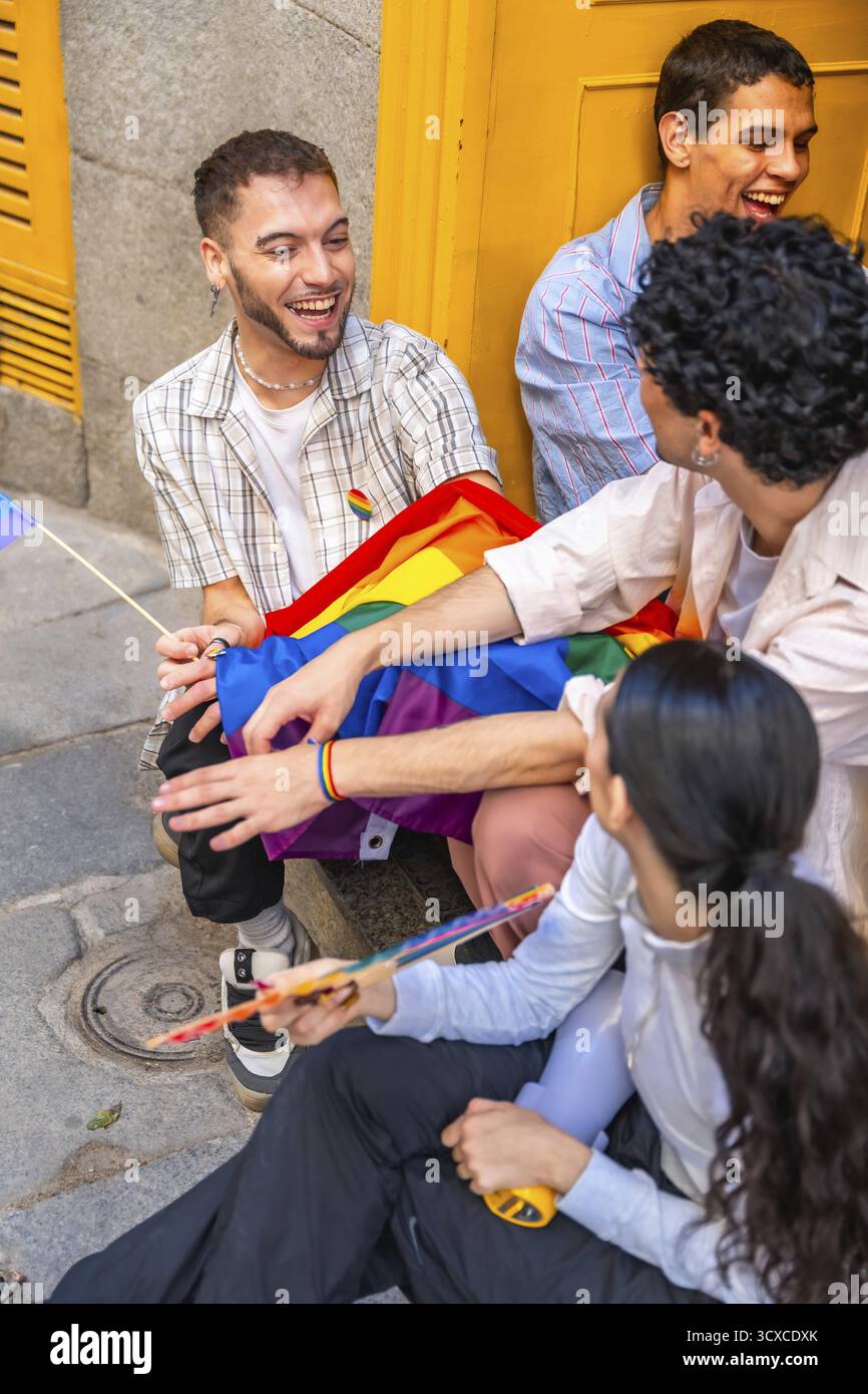 Gen z Freunde aus verschiedenen Hintergründen lachen und nehmen eine Regenbogenfahne im Freien an, feiern lgbtq plus Stolz, Inklusion und fröhliches miteinander Stockfoto
