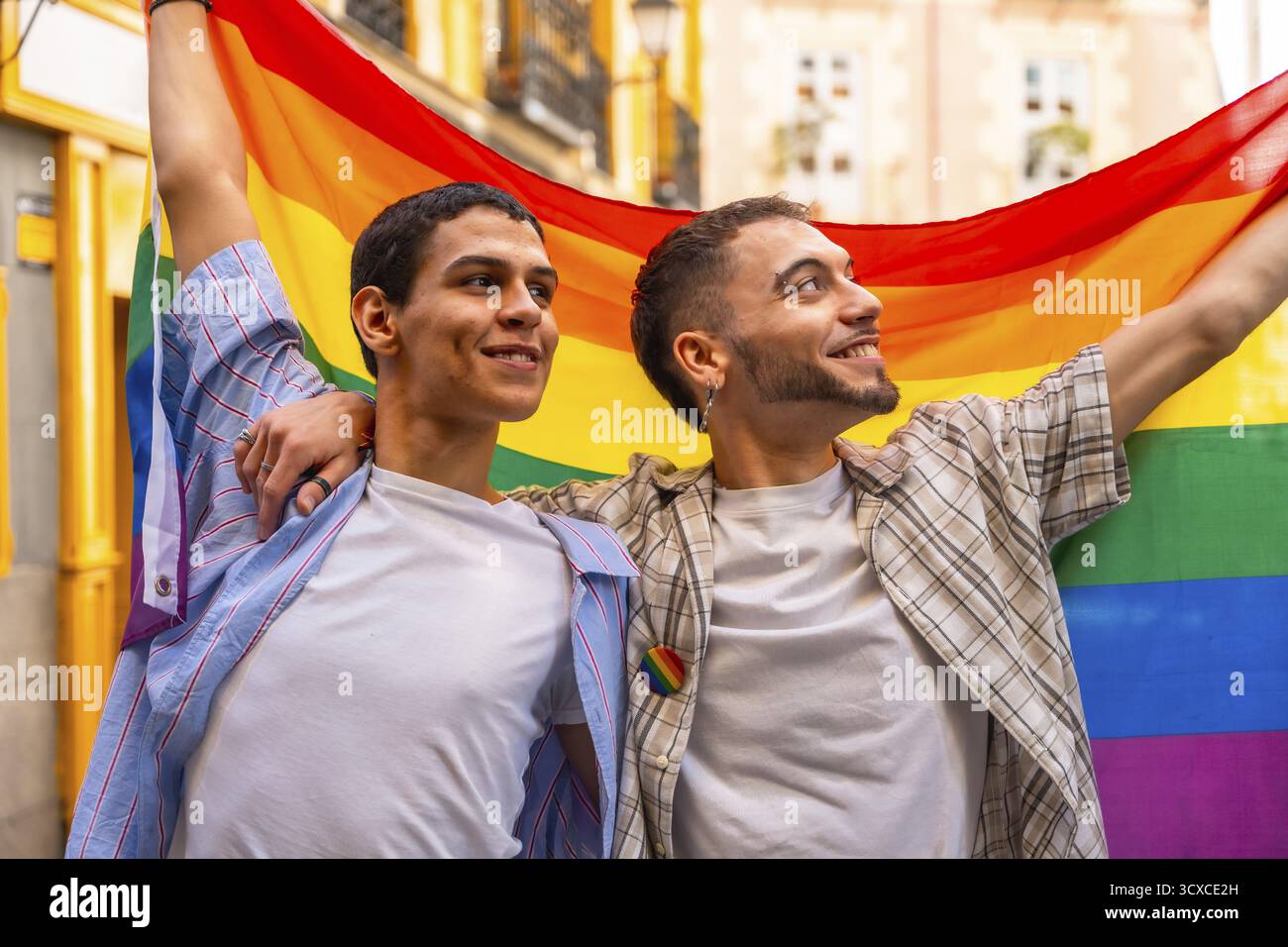 Zwei lächelnde Männer umarmen und zeigen stolz die leuchtende Regenbogenfahne, die lgbtq sowie Rechte, Liebe und Vielfalt während eines öffentlichen Dämons symbolisiert Stockfoto