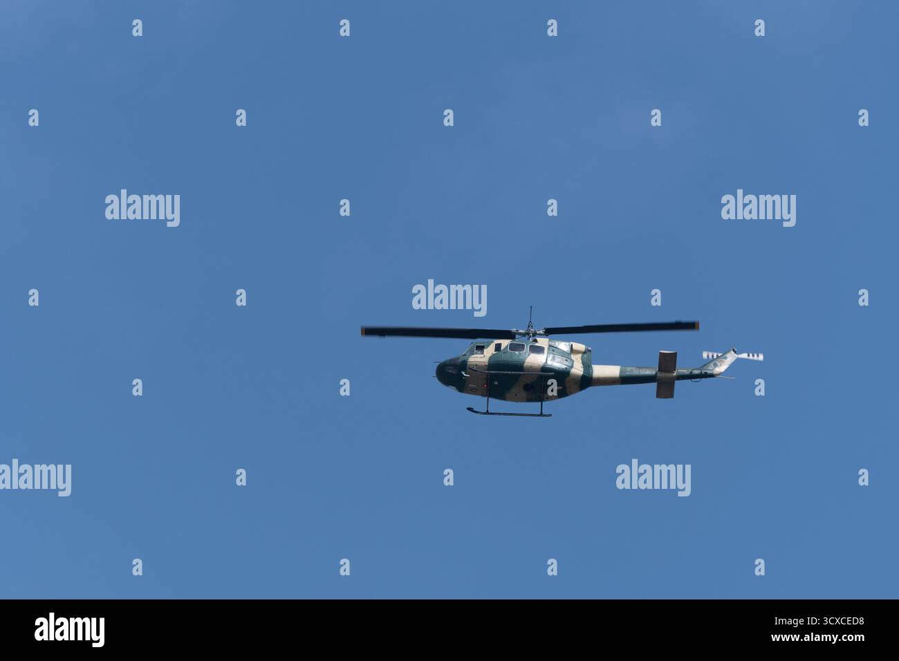 Ein Bell 212 Hubschrauber fliegt gegen einen klaren blauen Himmel. Der Hubschrauber ist in einem militärischen Tarnmuster gemalt. Stockfoto