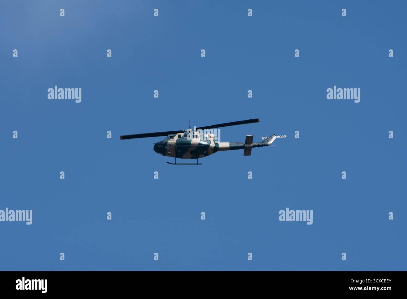 Ein Bell 212 Hubschrauber fliegt gegen einen klaren blauen Himmel. Der Hubschrauber ist in einem militärischen Tarnmuster gemalt. Stockfoto