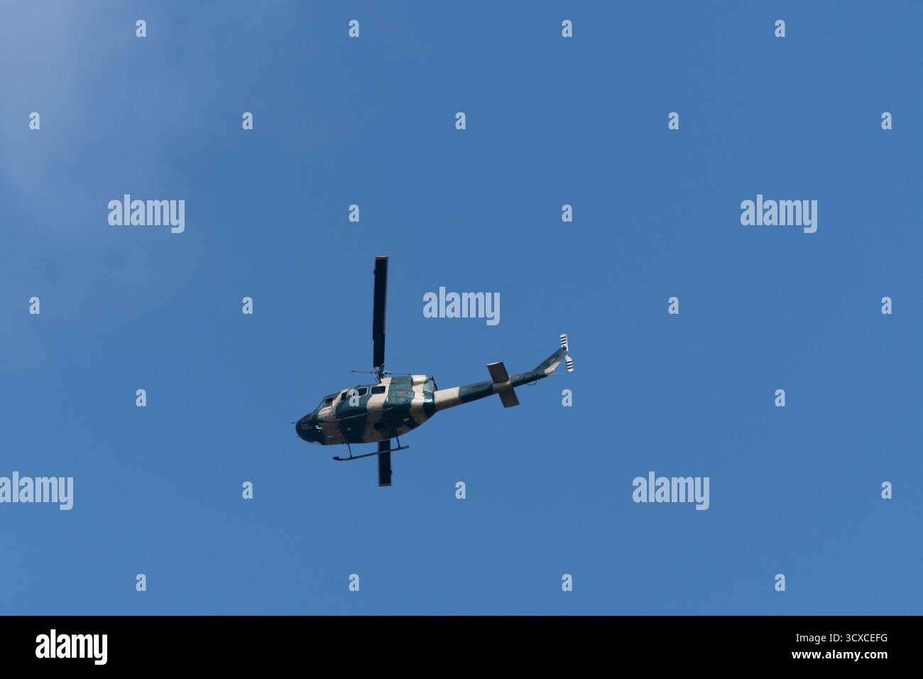 Ein Bell 212 Hubschrauber fliegt gegen einen klaren blauen Himmel. Der Hubschrauber ist in einem militärischen Tarnmuster gemalt. Stockfoto