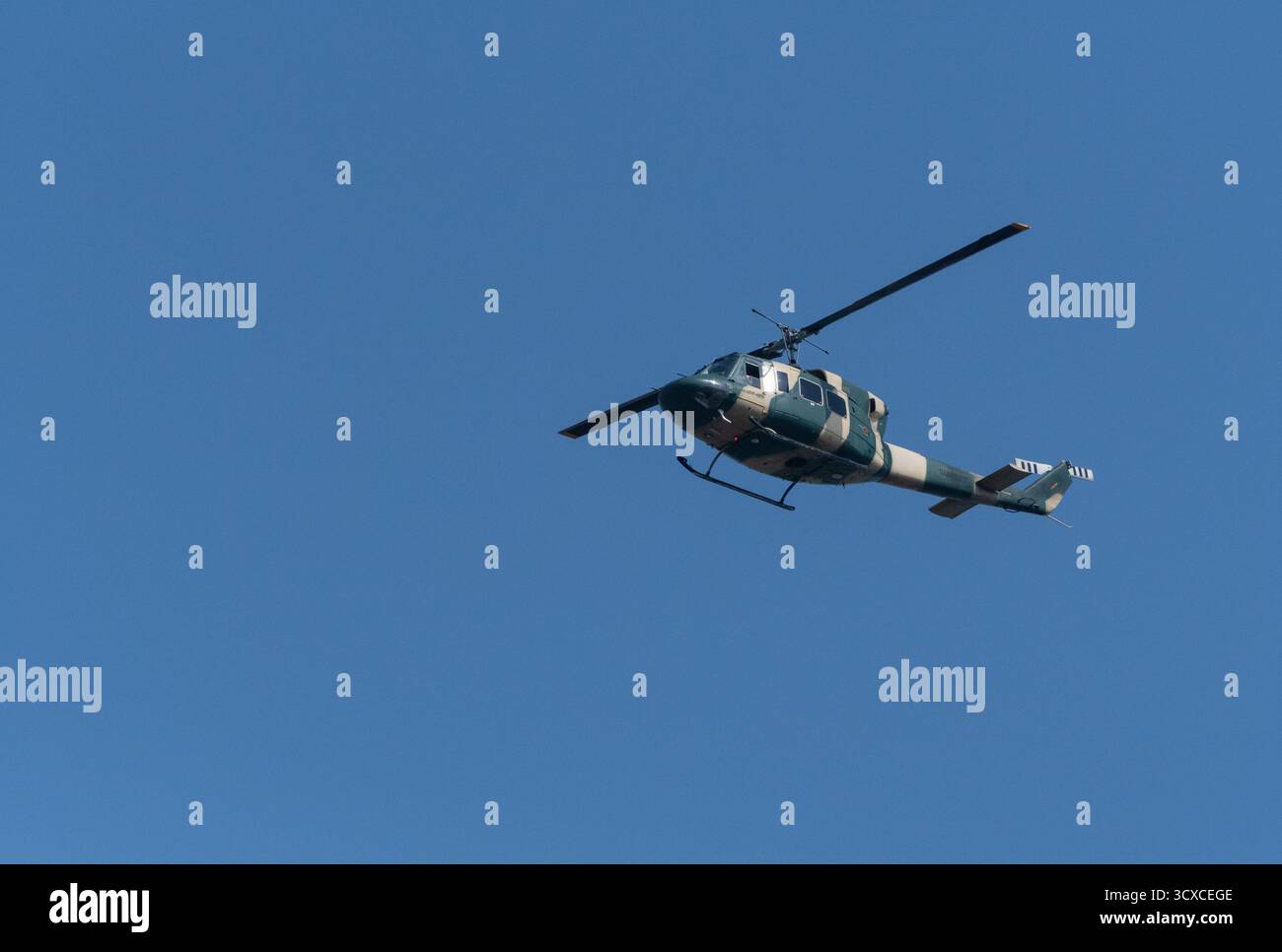 Ein Bell 212 Hubschrauber fliegt gegen einen klaren blauen Himmel. Der Hubschrauber ist in einem militärischen Tarnmuster gemalt. Stockfoto
