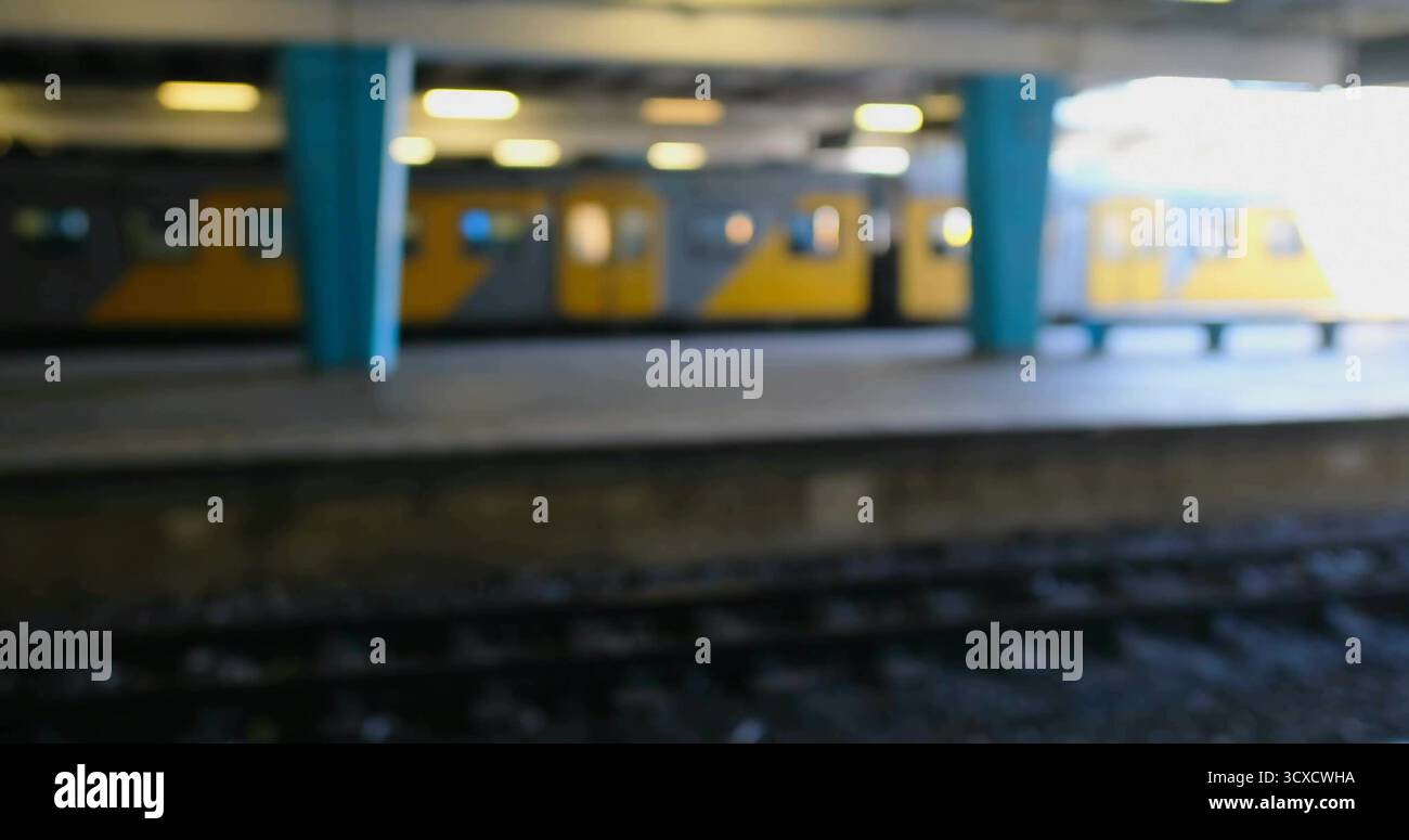 Gelber U-Bahn-Zug im Leerlauf auf dem Bahnsteig, mit blaugrünen Säulen, Deckenleuchten und Gleisen Stockfoto