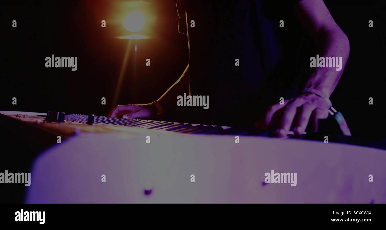 Er spielt einen erwachsenen männlichen Musiker mit elektronischer Tastatur in dimmem Studio, mit Scheinwerferlicht Stockfoto