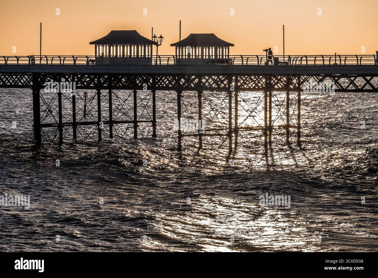 Silhouettenblick auf den Cromer Pier bei Sonnenaufgang mit Sonnenlicht, das auf dem Meer reflektiert Stockfoto
