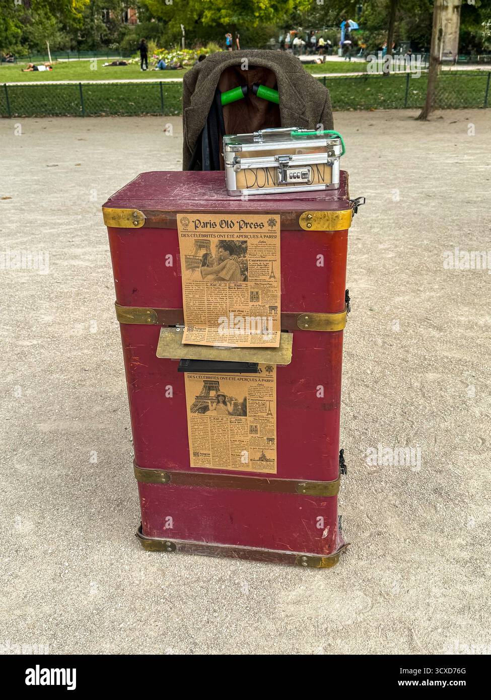 Vintage-Straßenfotostand in Paris mit rotem Kofferraum, alter Pressendekoration und sofortiger Kameraeinrichtung in einem Park. - Smartphone-aufgenommenes Stockfoto