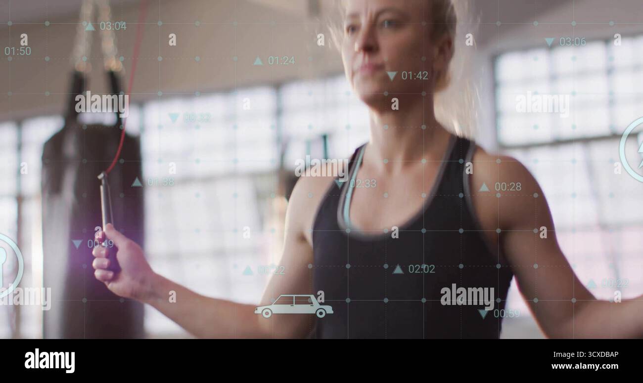 Überspringende Frau in schwarzer Sportbekleidung im Fitnessstudio, mit Sprungseil mit Boxsack und digitalen Overlays Stockfoto