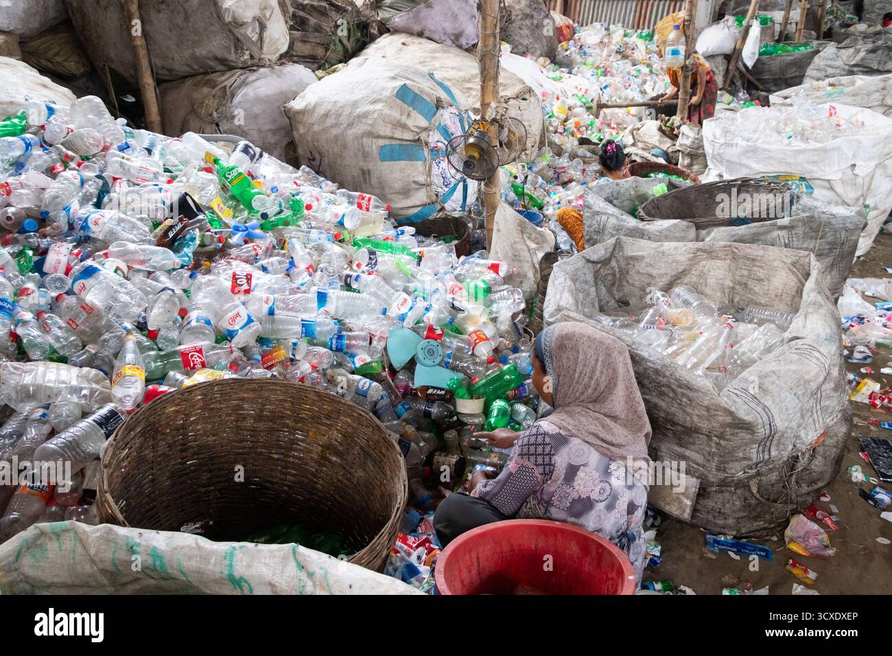Dhaka, Dhaka, Bangladesch. Oktober 2025. Arbeiter sortieren gebrauchte Plastikflaschen in einer Recyclingfabrik in Dhaka, Bangladesch. Sie tragen dazu bei, zu verhindern, dass die Flaschen entsorgt, auf Deponien verbracht werden, wo sie bis zu 1.000 Jahre für den biologischen Abbau benötigen oder verbrannt werden, wodurch giftige Dämpfe entstehen. Die Emissionen von CO2 und anderen Treibhausgasen werden verringert, wenn bei der Herstellung neuer Kunststoffe Recycling stattfindet. Quelle: ZUMA Press, Inc./Alamy Live News Stockfoto
