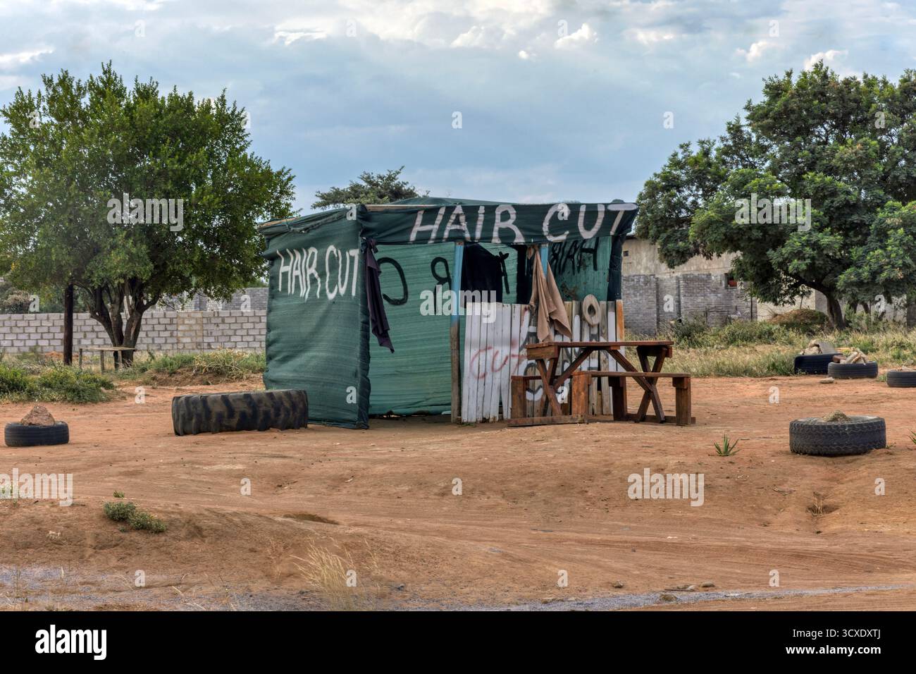 afrikanischer Friseurladen, Friseurladen in einer Hütte an der Schotterstraße auf der armen Seite der Stadt, Hütte mit grünem Schatten in Gaborone, Stockfoto