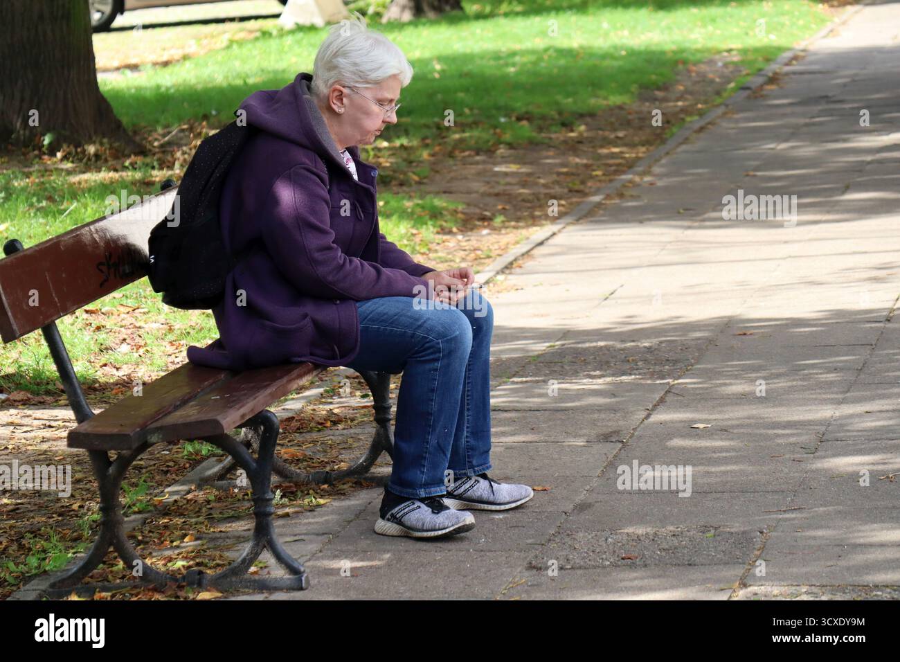 Ältere Frau, die allein auf einer Parkbank sitzt, in der Besinnung Stockfoto